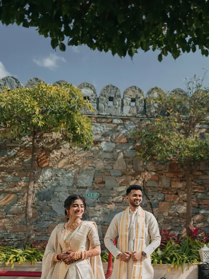 A beautiful portrait of the couple in their elegant South Indian Haldi attire, sharing a happy moment against a rustic stone wall.