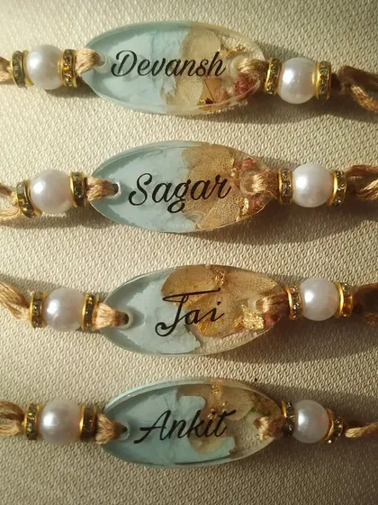 This set of custom name rakhis features a beautiful pastel blue background inside the resin. The names Sagar, Jai, and Ankit are written in an elegant script, complemented by delicate flowers, making each piece special.