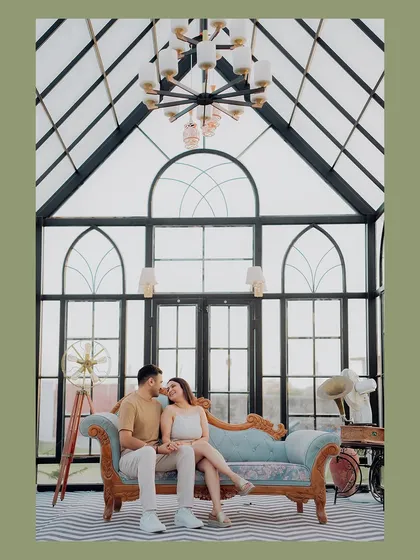A wide shot of the couple in the elegant glasshouse, capturing the full beauty of the location and their romantic pose.