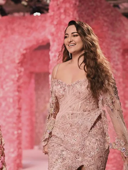 A candid moment of Sonakshi Sinha on the runway, her smile illuminated by the soft pink glow of the floral set. The environment was designed to evoke joy and romance, perfectly complementing the mood of the show.