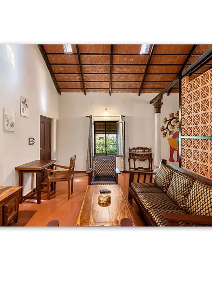 The living area of a plantation cottage, with traditional wooden furniture and a decorative terracotta screen. The space is cozy, rustic, and reflects the cultural heritage of the region.