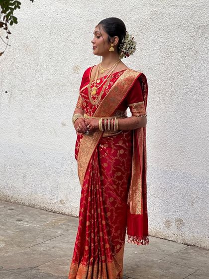 A side profile of a bride in her red brocade saree, showcasing the elegant drape and the intricate hairstyle adorned with fresh flowers.
