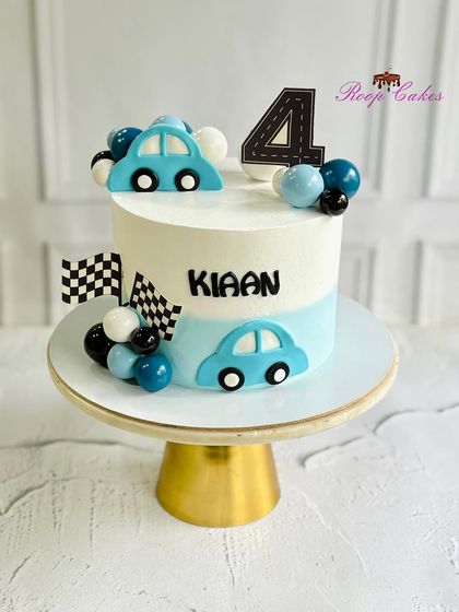 Zooming into four. A clean and modern car-themed cake for Kiaan's 4th birthday, decorated with blue cars, checkered flags, and balloon-like spheres.