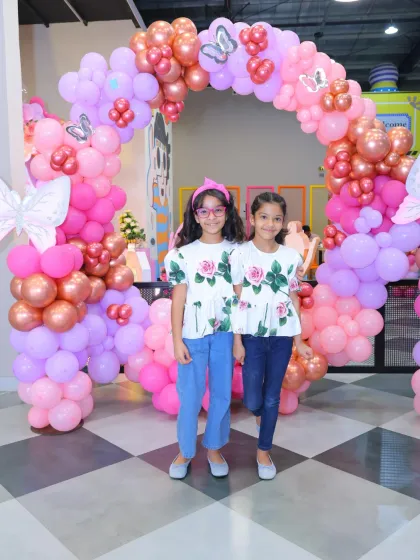Two friends pose in front of a beautiful butterfly-themed balloon arch. The pink and rose gold colors create a delicate and magical atmosphere.