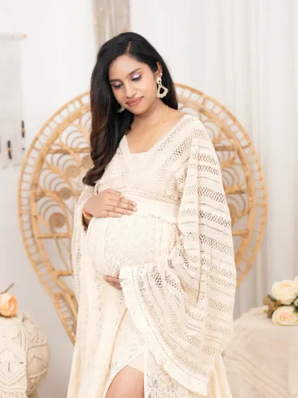 A soft and gentle portrait of a mother-to-be in a boho-style lace dress. The natural textures of the rattan chair and macrame decor create a warm and earthy vibe.