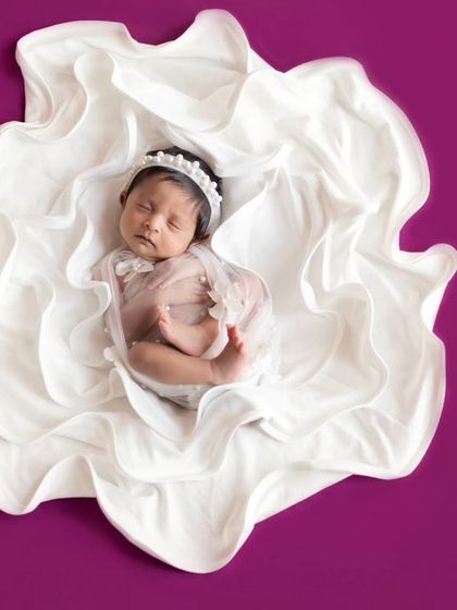Like a precious pearl in a flower. This creative shot uses white fabric to create a blooming effect around the sleeping newborn.