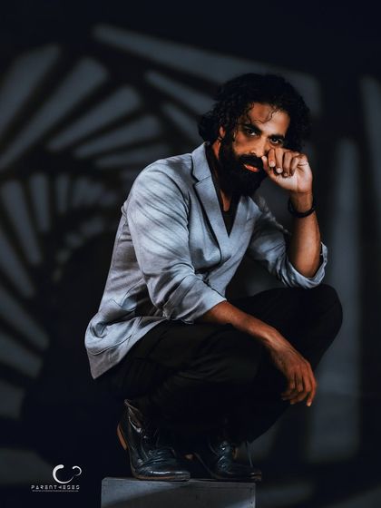 A close-up, intense portrait where the subject's gaze pierces through the shadows. The hand gesture adds a layer of mystery and contemplation.