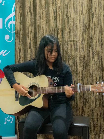 A student plays her acoustic guitar using a capo, demonstrating different techniques taught in class.