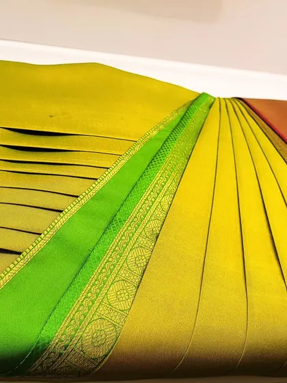 A close-up of the pleats on a yellow and green silk saree, showing the neat finish.