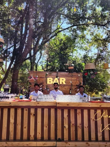 Meet the team ready to make your event a hit. Our professional bartenders are set up and ready to serve at this beautiful outdoor wedding, standing behind a custom-built rustic wooden bar.