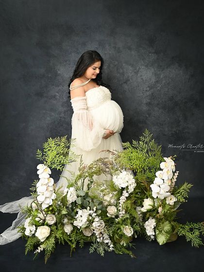 A garden of white. The mom-to-be stands amidst a beautiful arrangement of white flowers and greenery, creating a fresh and pure portrait.