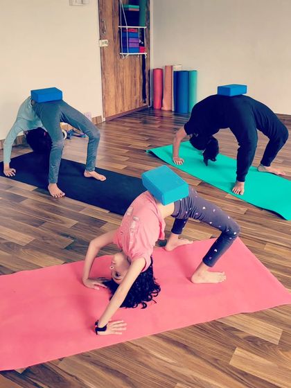 We love using props to make challenging poses more fun. Here, my students are using yoga blocks to help with alignment and stability in Chakrasana, or wheel pose, turning a difficult backbend into a playful challenge.