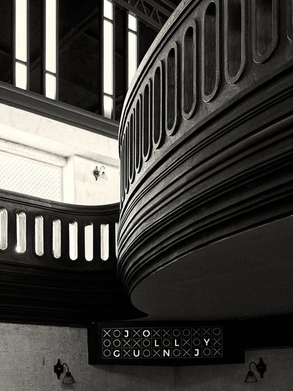 The curved wooden balustrade of the mezzanine, with a custom "JOLLYGUNJ" sign below. This shot emphasizes the strong, sculptural lines of the interior architecture.