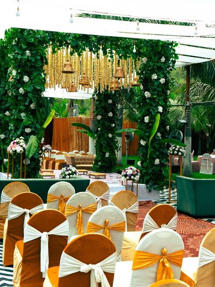 A beautiful mandap setup with a focus on greenery and traditional elements. The pillars are covered in lush leaves, and hanging temple bells add a divine and serene touch to the ceremony.