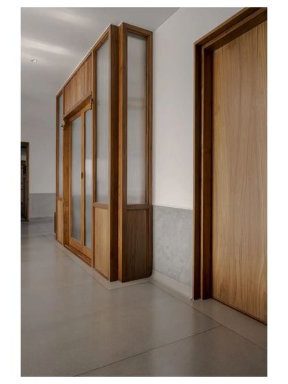 A hallway where the in-situ terrazzo floor climbs partway up the wall, creating a durable and visually continuous wainscoting. This detail is juxtaposed with the warmth of the teak door and fluted glass panels.