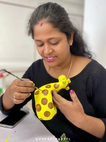 A mother carefully paints brown spots on a bright yellow giraffe planter, enjoying a creative moment for herself.
