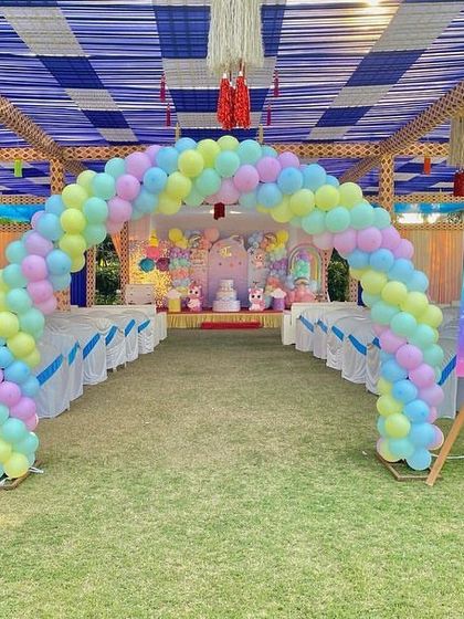 A grand unicorn party entrance in an outdoor setting. A pastel rainbow balloon arch welcomes guests to the celebration, with a themed welcome sign on an easel.