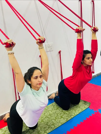 Using the wall ropes for support in a kneeling backbend helps to build upper body strength and open the shoulders, preparing the body for deeper postures.
