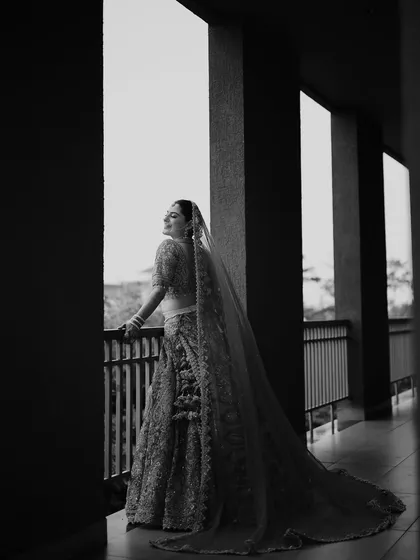 A stunning black and white bridal portrait. The bride stands on a balcony, her long veil trailing behind her, creating a powerful and elegant silhouette.