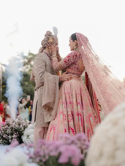 A moment of gentle affection during the varmala ceremony. The pastel floral decor and the soft, diffused light enhance the tenderness of this interaction, a key moment in their wedding story.