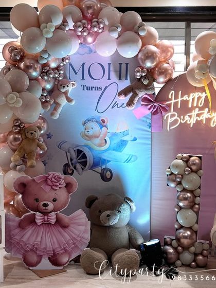 A close-up of our teddy bear themed first birthday setup, showing the custom backdrop with the baby's name, 'Mohi'. The decor includes a balloon arch, teddy bear props, and a 'Happy Birthday' neon sign.