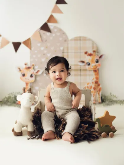 A happy baby in a neutral outfit smiles for the camera during his giraffe-themed sitter session.