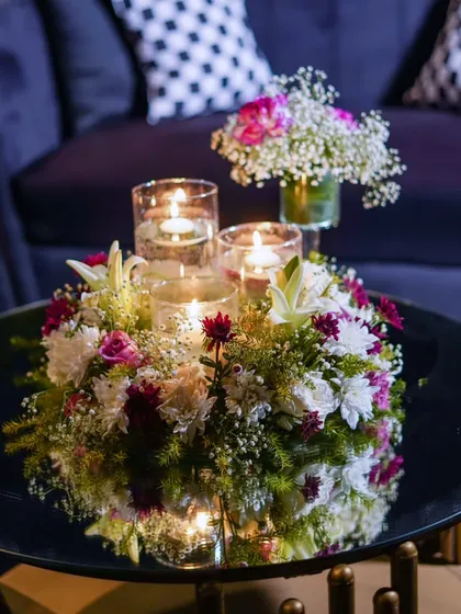 A centerpiece detail, where floating candles in glass cylinders are nestled within a lush arrangement of white and pink flowers on a mirrored coffee table.