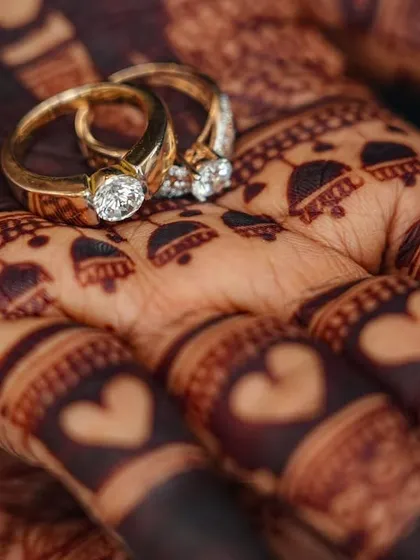 Another artistic close-up of the engagement rings on the palm. The intricate details of the henna, including the tiny hearts on the fingers, are clearly visible.