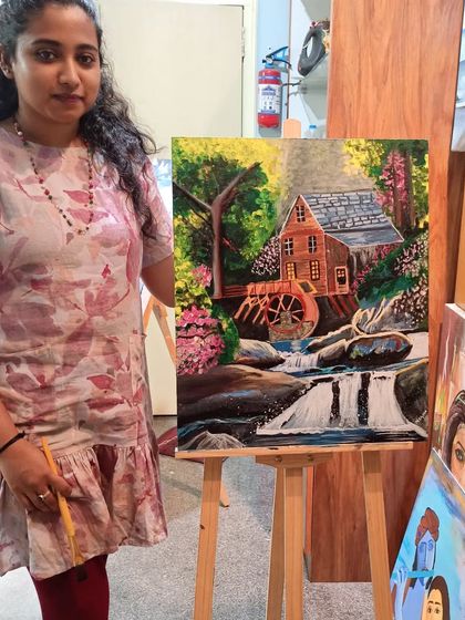 Megha Shree proudly stands with her completed landscape painting. This piece, featuring a rustic house by a waterfall, is a testament to the skills she developed during her acrylic painting course.