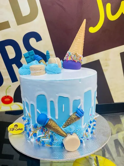 This light blue drip cake is decorated with an upside-down ice cream cone, macarons, and smaller edible cone details. The base is sprinkled with blue and white nonpareils, creating a fun and festive look for any birthday.