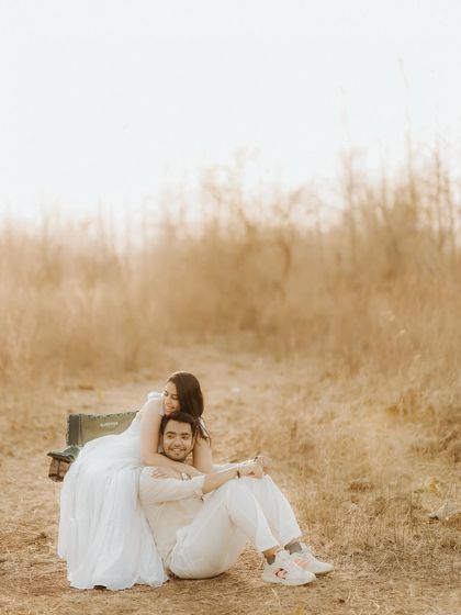 A relaxed and happy portrait in a golden field. The bride leans on her partner's back, sharing a comfortable and affectionate moment during their outdoor pre-wedding shoot.