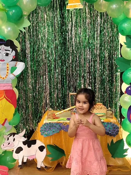 A little girl dressed for the occasion poses at our Janmashtami celebration. Our themed decor, featuring Krishna, cows, and peacocks, creates an immersive and picture-perfect environment for the festival.