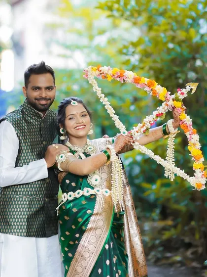 A playful outdoor shot of the couple with a floral bow and arrow, a traditional prop used in Dohale Jevan ceremonies to symbolize the fulfillment of the mother-to-be's wishes.