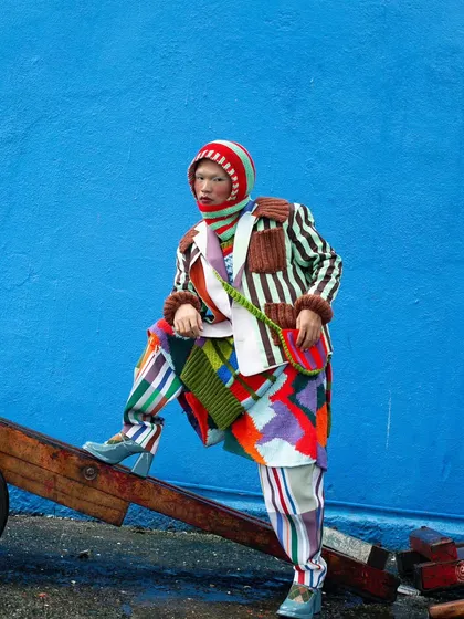 Using the environment to create a dynamic pose. This image from the "Kaleidoscope" series shows the model interacting with a wooden cart, adding a layer of narrative to the vibrant, multi-patterned outfit.