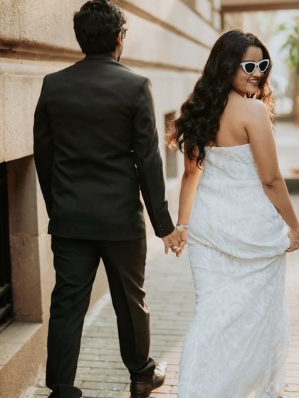A candid "follow me" shot through the streets of Mumbai, highlighting the bride's chic white gown and playful sunglasses.