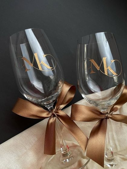 'Tis the season for gifting. A pair of wine glasses with bold, gold-filled engraved monograms, tied with satin ribbons, ready to be gifted as wedding favors.