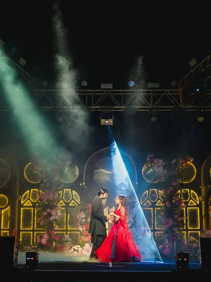 The couple on stage under a single spotlight, creating a dramatic and romantic moment during their Sangeet performance.