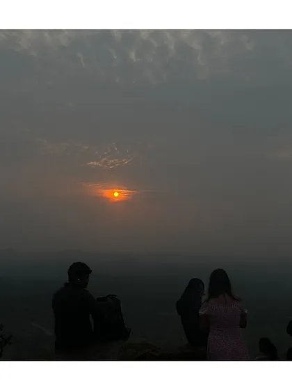 A serene sunrise moment from the Huthridurga trek, with a few people watching the sun come up.