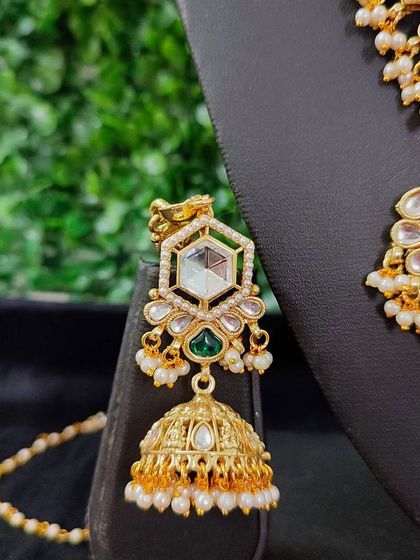 This close-up shows the earring from the hexagonal-motif bridal set. The design features a large polki stone, green accent stone, and a classic jhumka drop.
