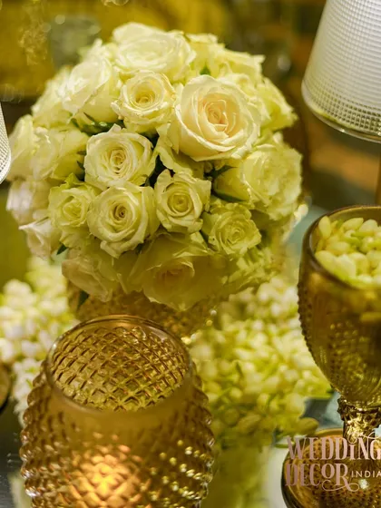 A close-up of the white rose bouquet, surrounded by the warm glow of textured gold candle holders. This highlights the romantic and classic elements of the tablescape.