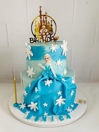 A magical two-tier Frozen cake featuring a beautiful fondant dress for Elsa, surrounded by shimmering snowflakes.