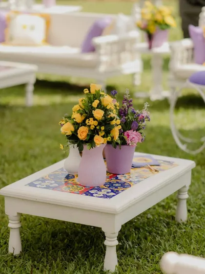 A custom-designed coffee table with a beautiful mosaic tile top, part of the lounge seating at the pastel Haldi. The fresh flowers in a lavender vase perfectly complement the color scheme.