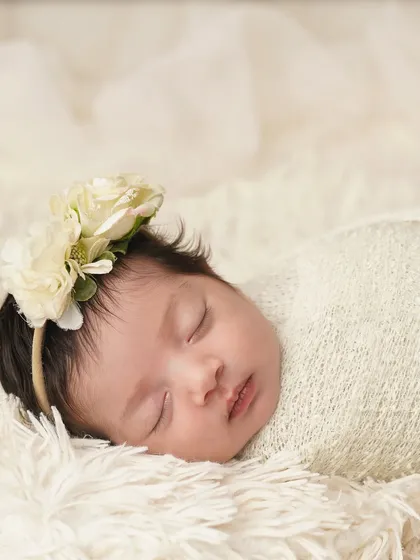 A close-up of a newborn girl swaddled and sleeping on a fluffy white blanket, adorned with a floral headband. This classic shot is all about capturing their angelic peace.