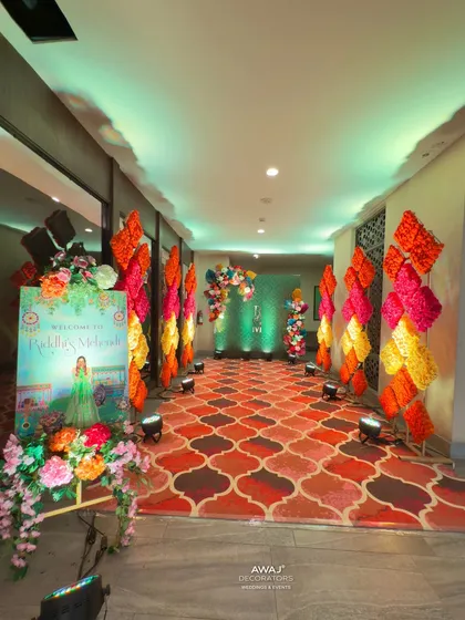 A colorful walkway for an indoor Mehendi, with a patterned carpet and vibrant floral stands guiding the way.