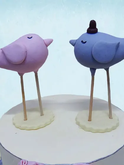 A close-up of the adorable lovebird toppers on our first anniversary cake, one wearing a tiny hat.