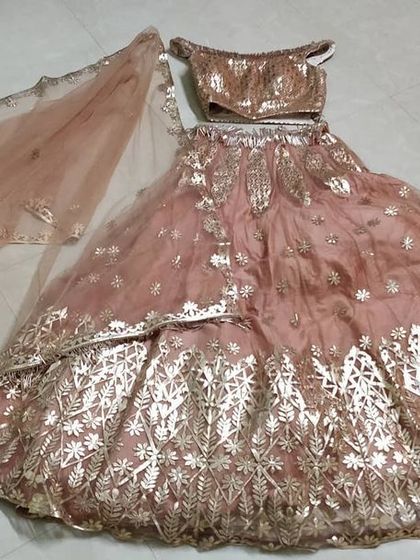 A flat-lay of the peach off-shoulder lehenga set. This view shows the coordination between the blouse, skirt, and sheer dupatta, all featuring beautiful gold work.