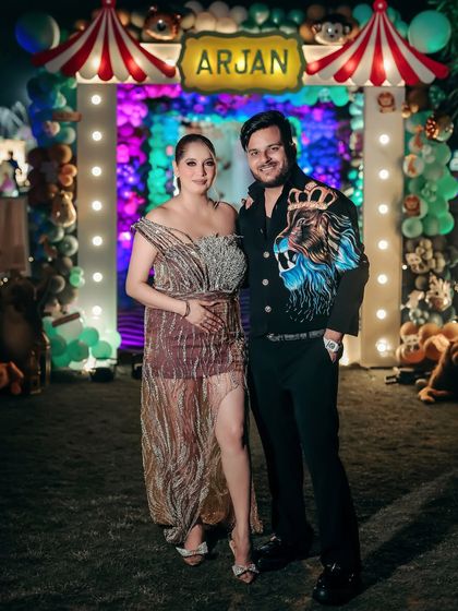 A full-length shot of the expecting couple at their celebration. The colorful balloon arch and festive lights create a vibrant and joyful backdrop for their maternity portrait.
