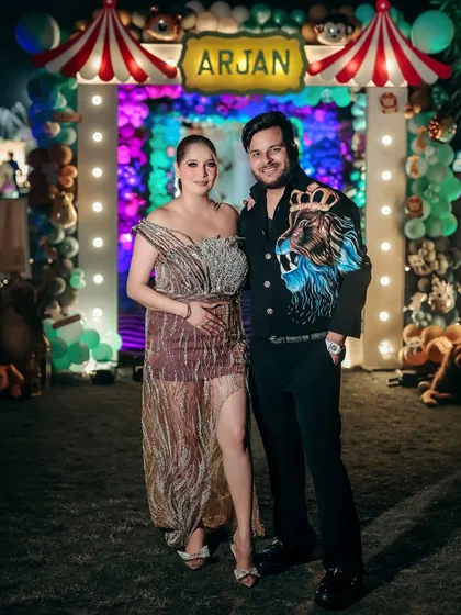 A full-length shot of the expecting couple at their celebration. The colorful balloon arch and festive lights create a vibrant and joyful backdrop for their maternity portrait.