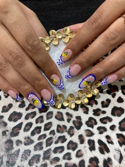 An example of our detailed, hand-painted nail art. These stiletto-shaped extensions feature a modern French tip design with a blue checkerboard pattern, accented with delicate yellow floral paintings for a unique and artistic finish.