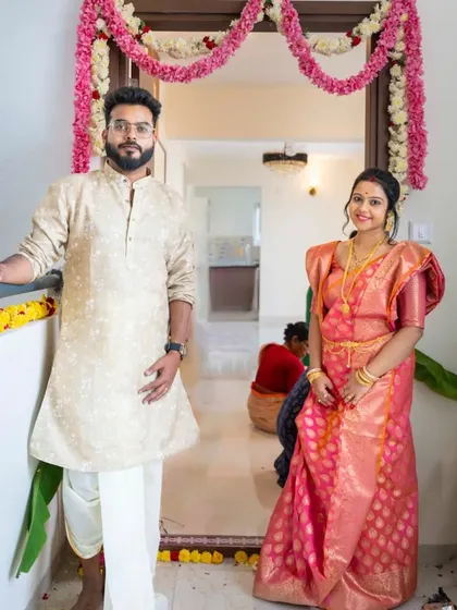 A proud moment for a new beginning. This couple stands at the doorway of their new home during their Gruha Pravesh ceremony, dressed in beautiful traditional attire. This classic portrait captures the significance and happiness of starting a new chapter together.
